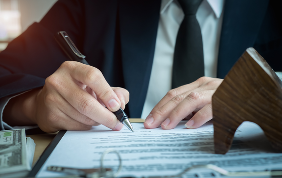 Person in a suit signing a contract; house model and money nearby.