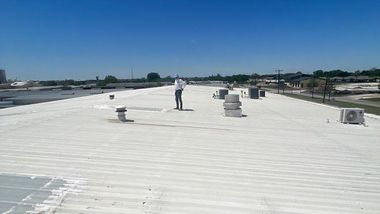 Man stands on a white commercial roof with vents, under a blue sky.