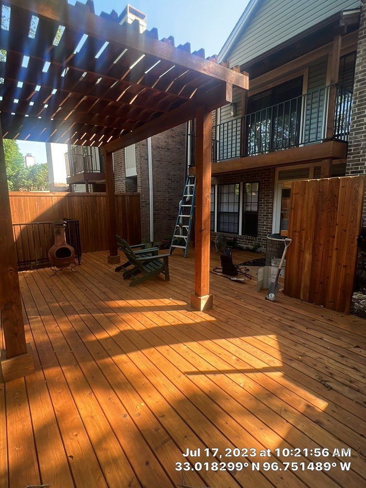 Wooden deck with pergola, fence, and chairs in a backyard setting.