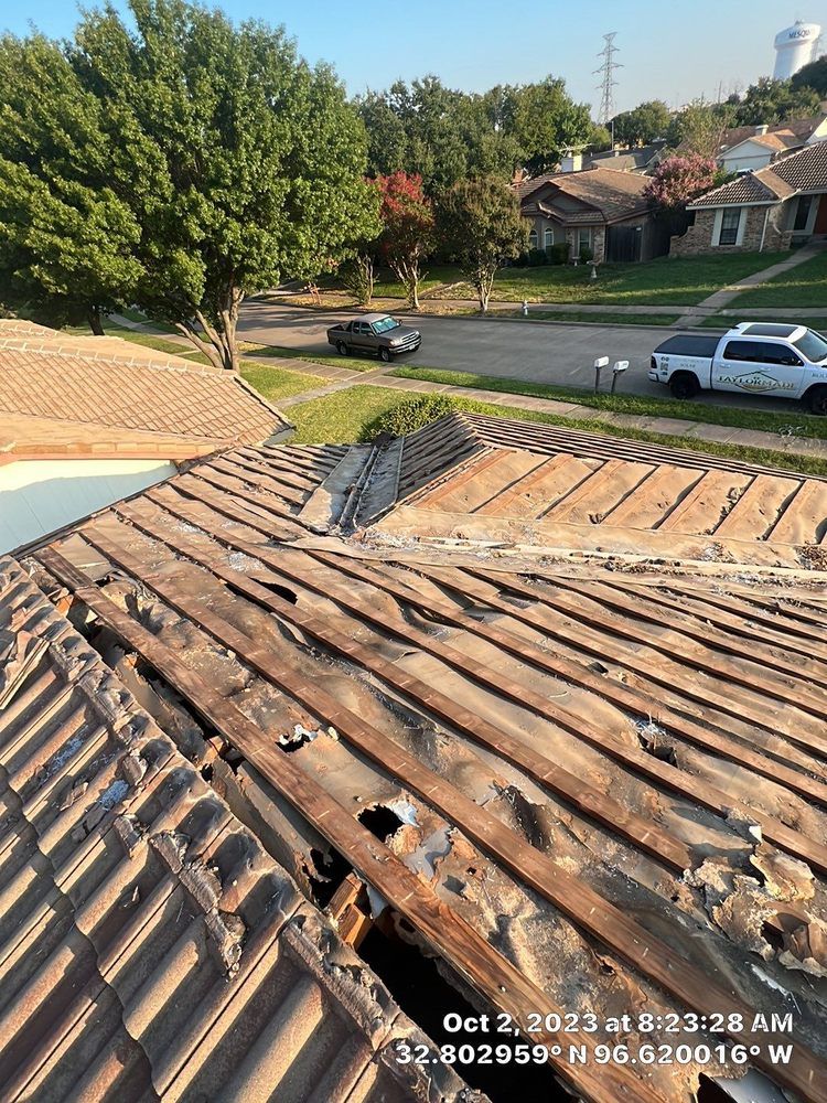 Damaged terracotta tile roof with exposed wood in a residential neighborhood.