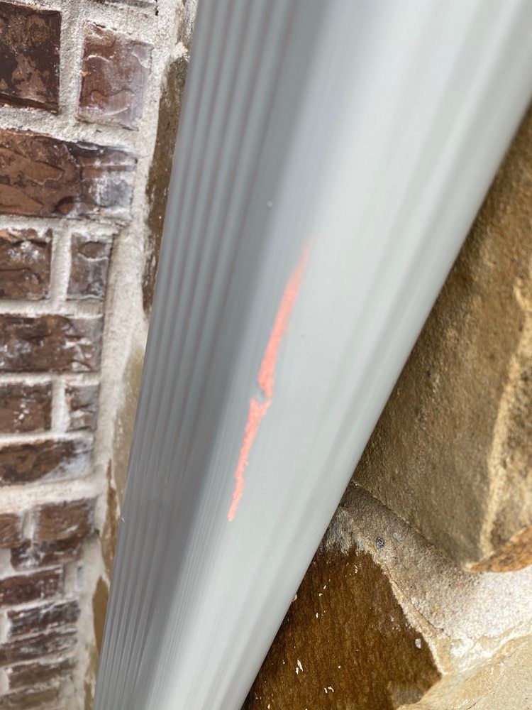 A light gray gutter with a crack marked in orange against a brown brick wall.
