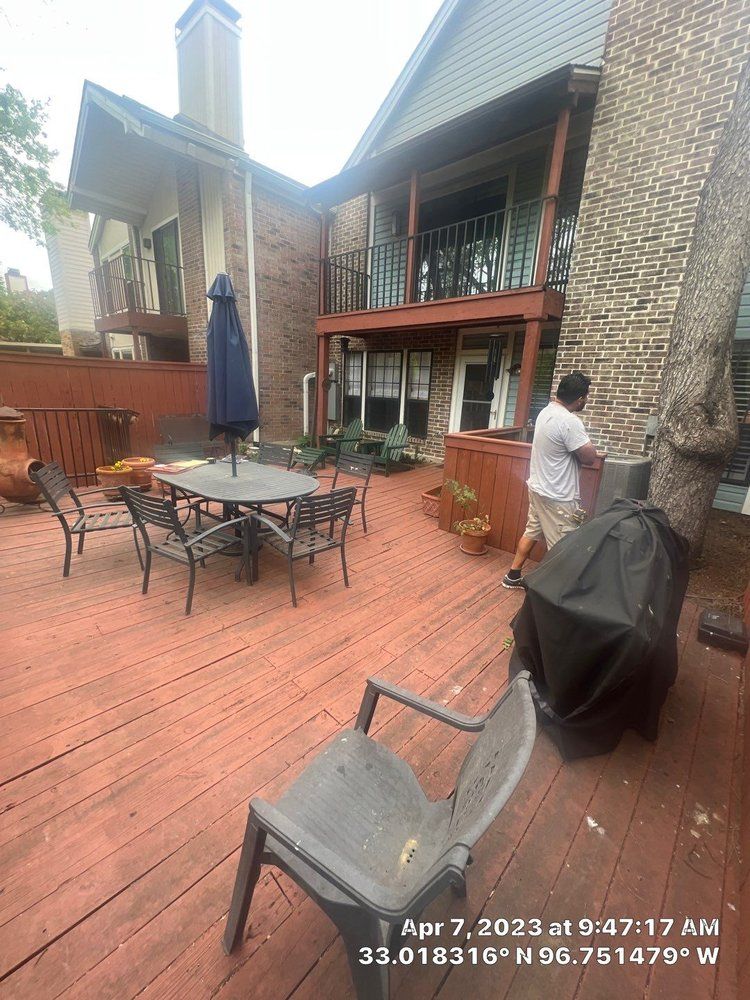 A backyard deck with furniture, a grill, and a person. Building and a tree are in the background.