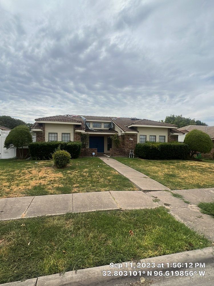 A one-story brick house with a tiled roof and manicured bushes under a cloudy sky.
