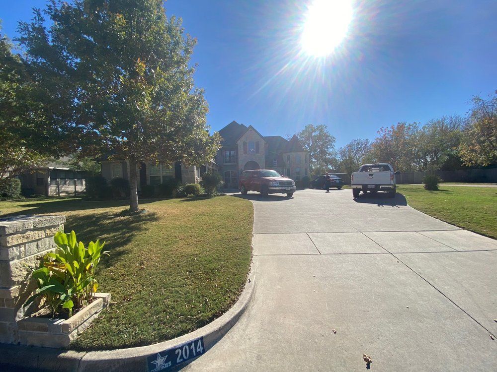 A large house with a driveway, cars, and lawn under a bright sun.