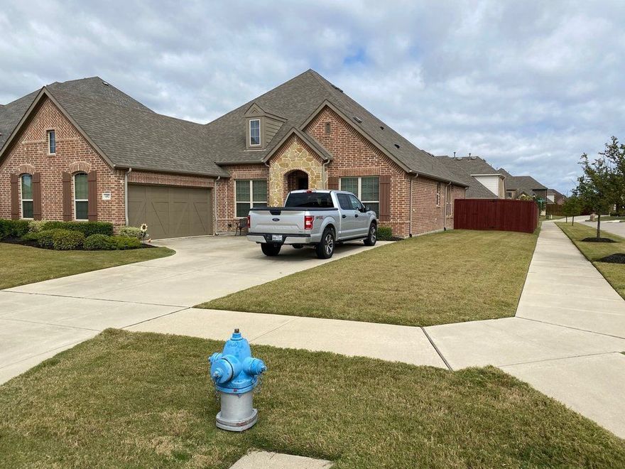 Silver pickup truck parked in front of a brick house with a lawn and blue fire hydrant on a cloudy day.