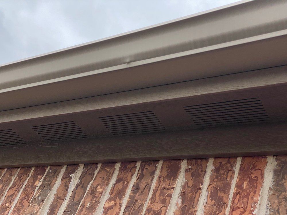 Tan soffit and gutter over a brick wall, with a cloudy sky visible.