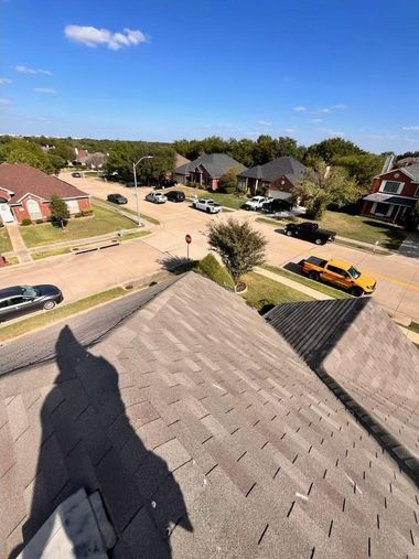 View from a rooftop overlooking a residential street with houses, cars, and a clear blue sky.