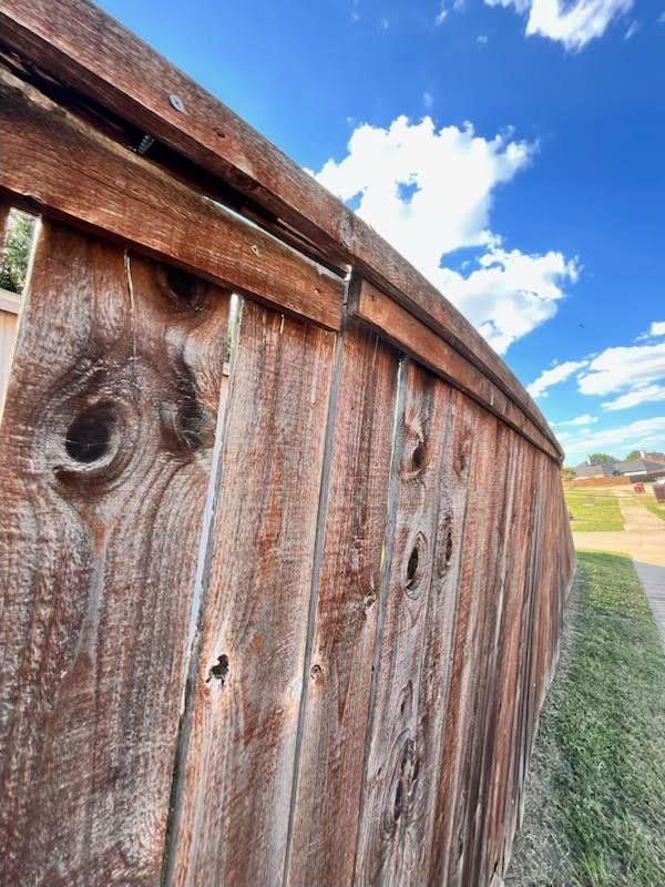 Wooden fence curving against a blue sky with fluffy white clouds.