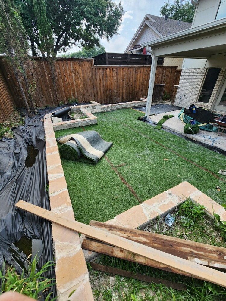 Backyard with artificial turf installation in progress; stone borders and wooden fence.