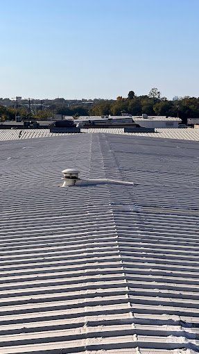 Flat commercial roof with rows of ribbed metal and a vent against a clear blue sky.