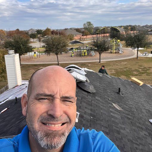 Man on a roof smiles for a selfie while another person works. A playground is in the background.