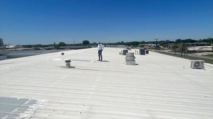 Man stands on a flat, white commercial roof under a clear blue sky.