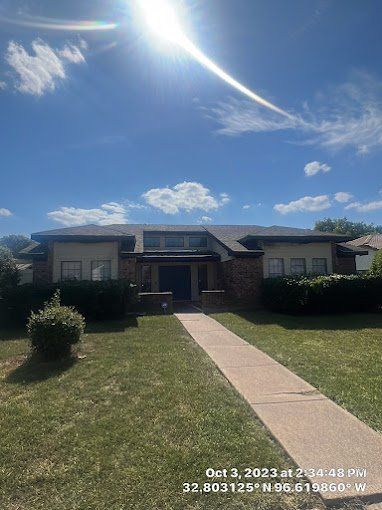 House with brick facade and dark roof under a bright blue sky. A sidewalk leads to the front door.