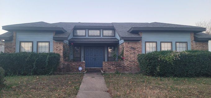 A two-story house with brick walls, blue accents, and a dark roof. A stone path leads to the blue front door.