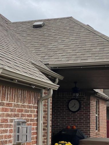 Brick house with gray roof, gutters, and a covered patio with a clock and grill.