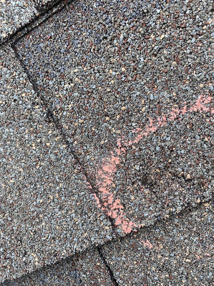 Close-up of gray asphalt shingles, with a pink chalk line indicating a possible repair.