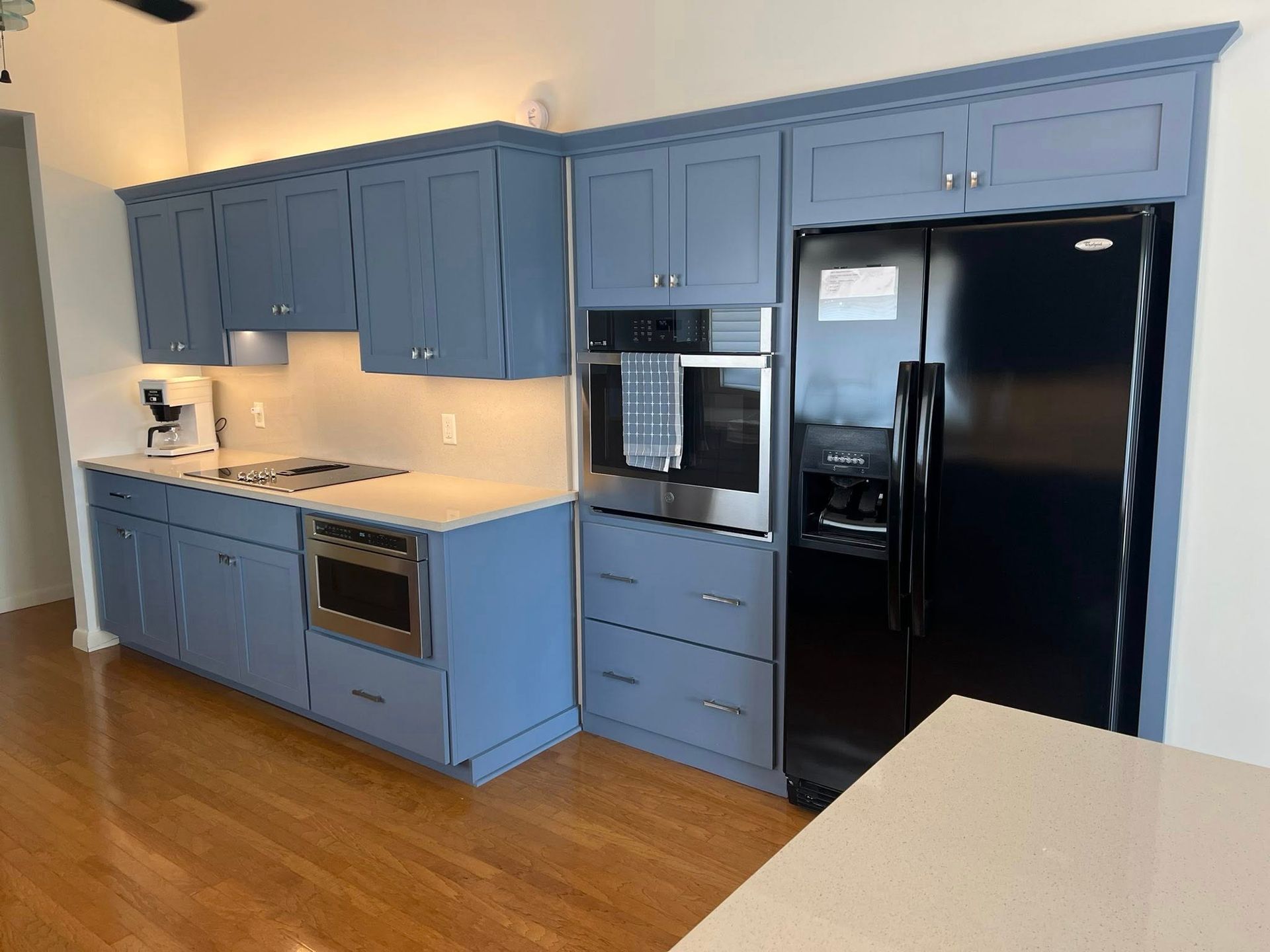 Blue kitchen with black appliances, wood floors, and a white countertop