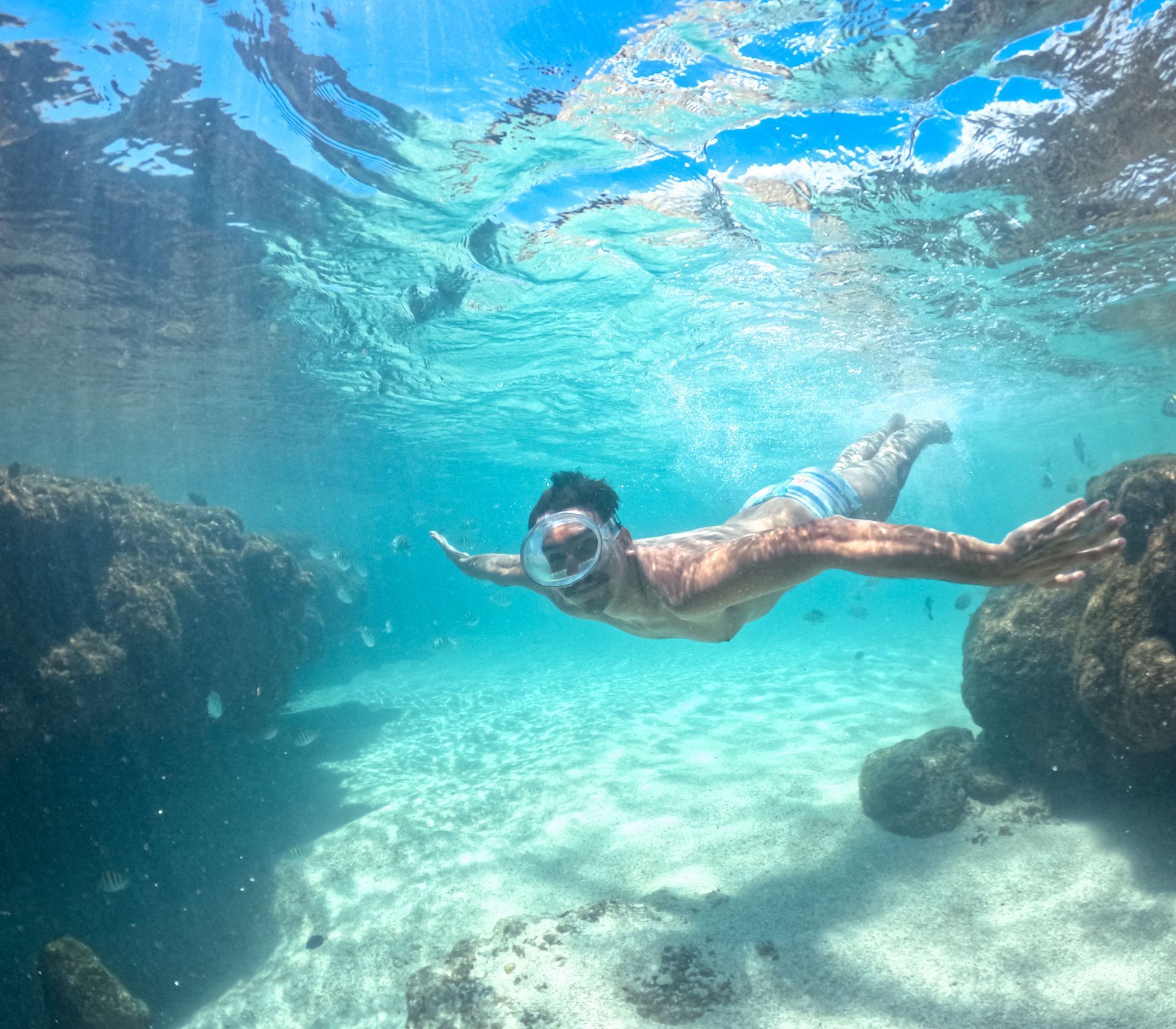 Homem mergulhando nas piscinas naturais de Proto de Galinhas, em meio aos peixes e corais.