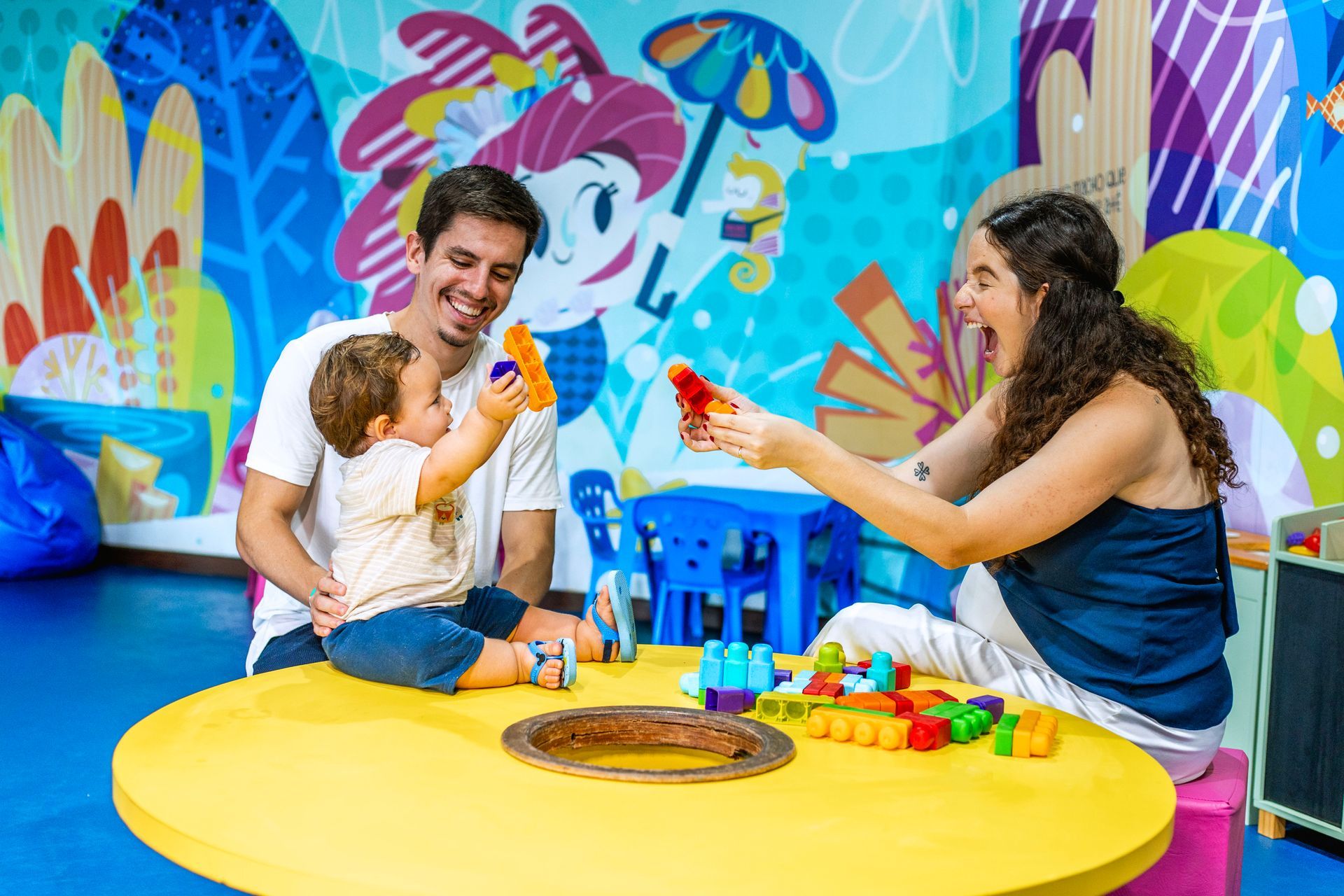 Família brinca com criança pequena em espaço infantil do Armação Resort.