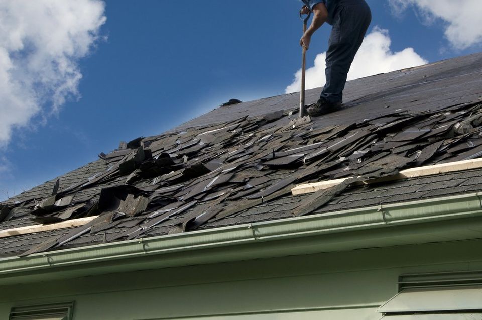 Man scrapping shingles off of a roof