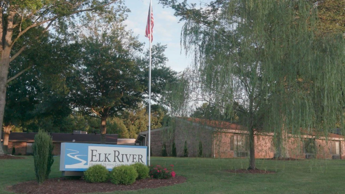 A sign for elk river is in the middle of a lush green field
