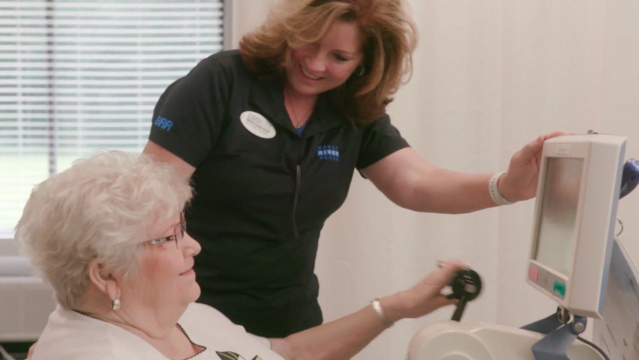 A nurse is helping an elderly woman use a computer.