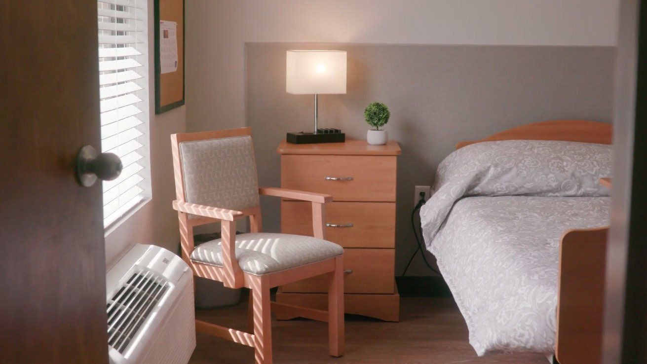 A bedroom with a bed , chair , dresser and lamp.