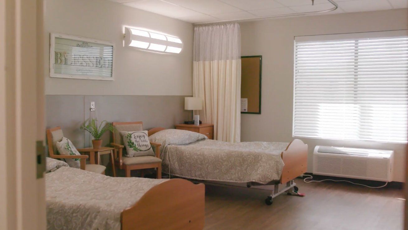 A hospital room with two beds , a chair and a window.