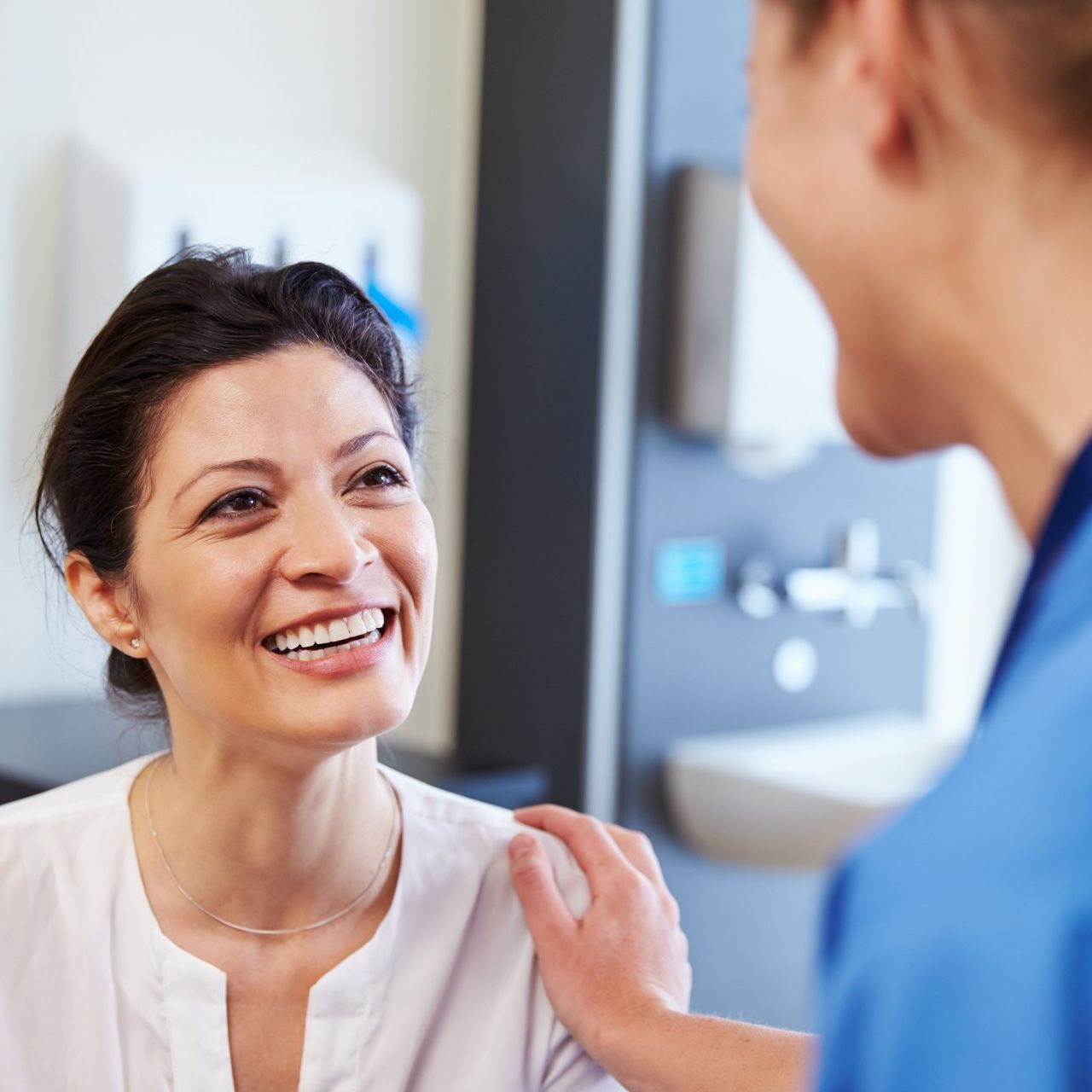 Woman smiles at a medical professional, who has a hand on the woman's shoulder, in a clinic setting.