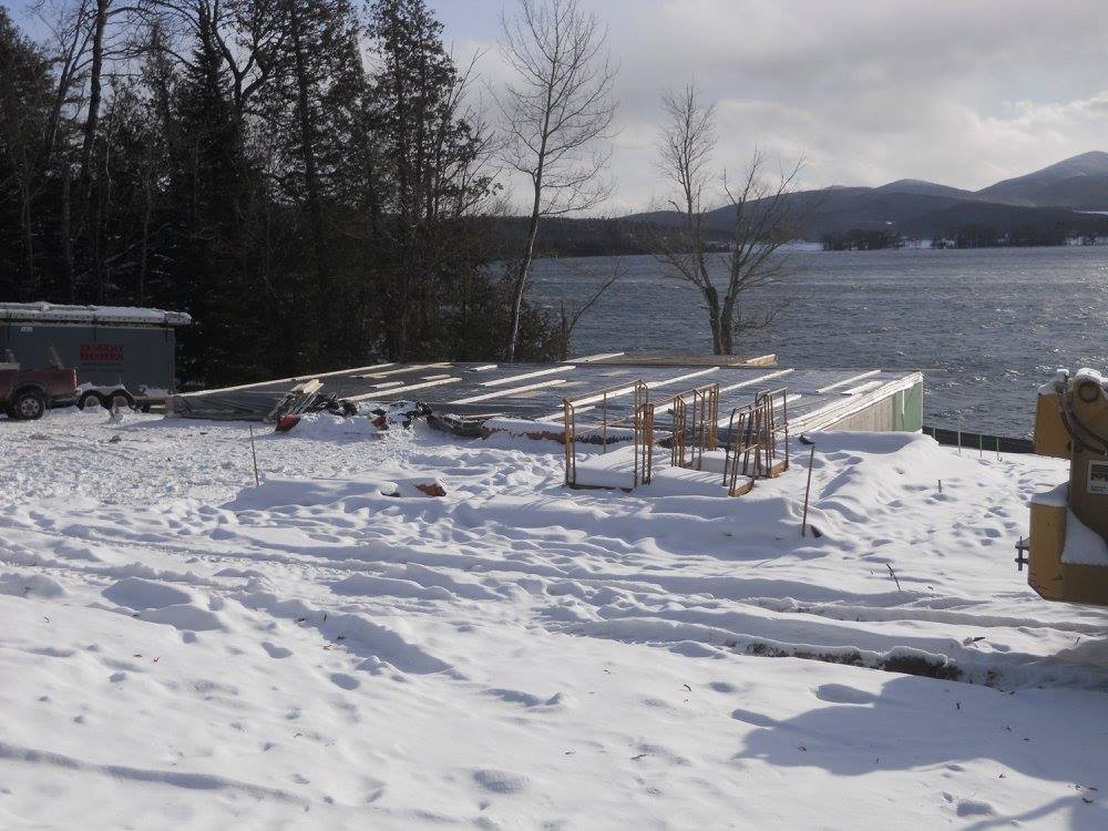 A snowy area with a few trees and a lake in the background