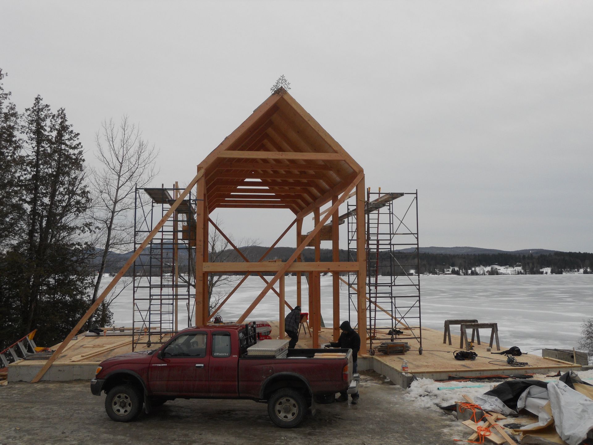 A red truck is parked in front of a wooden structure under construction