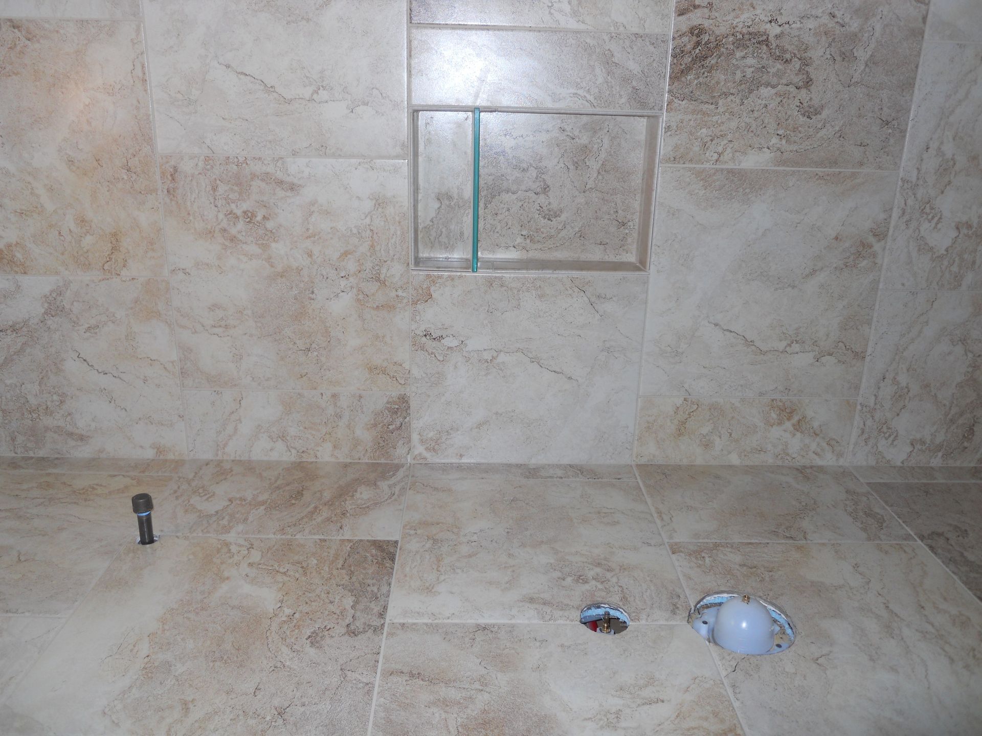 A bathroom with a tiled floor and a glass shower niche