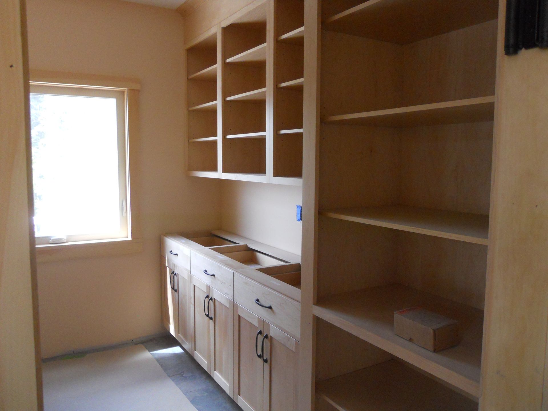 A kitchen with wooden cabinets and shelves and a window