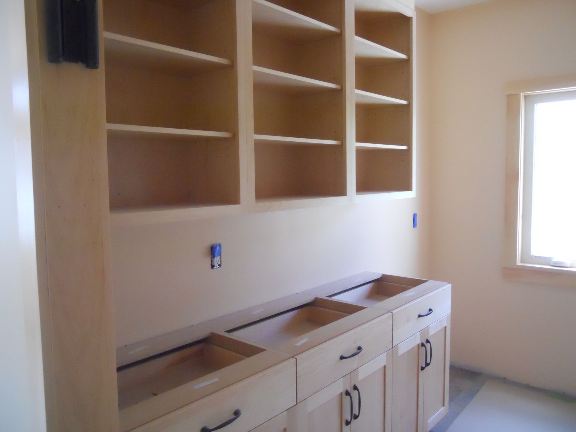 A kitchen with wooden cabinets and shelves and a window
