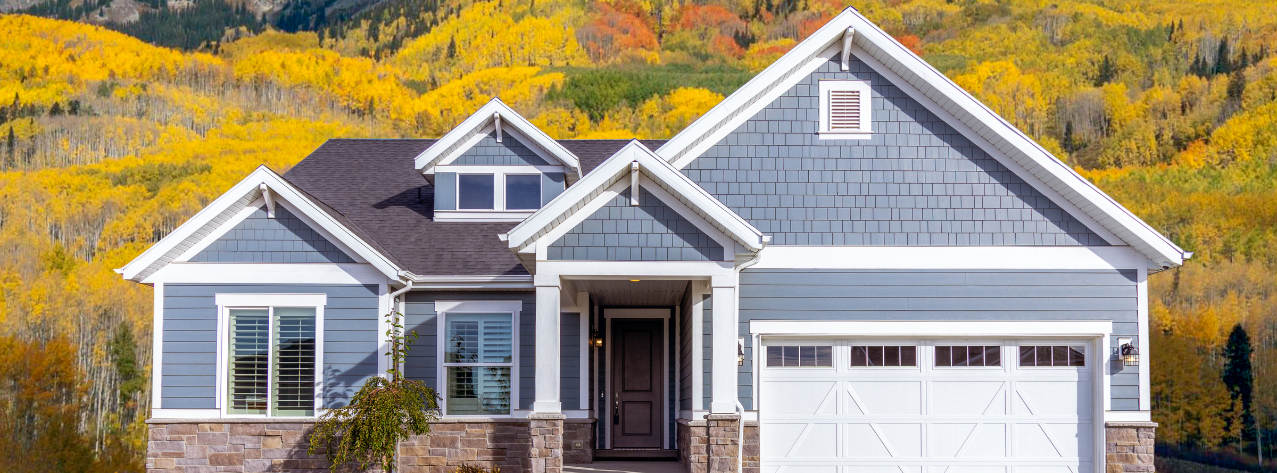 A blue house with a white garage door is surrounded by yellow trees in Vermont.