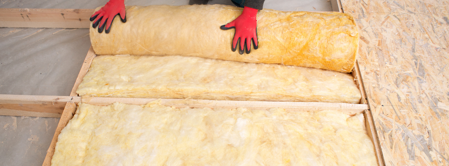 A Tanguay Homes contractor is rolling a roll of insulation on a wooden floor.