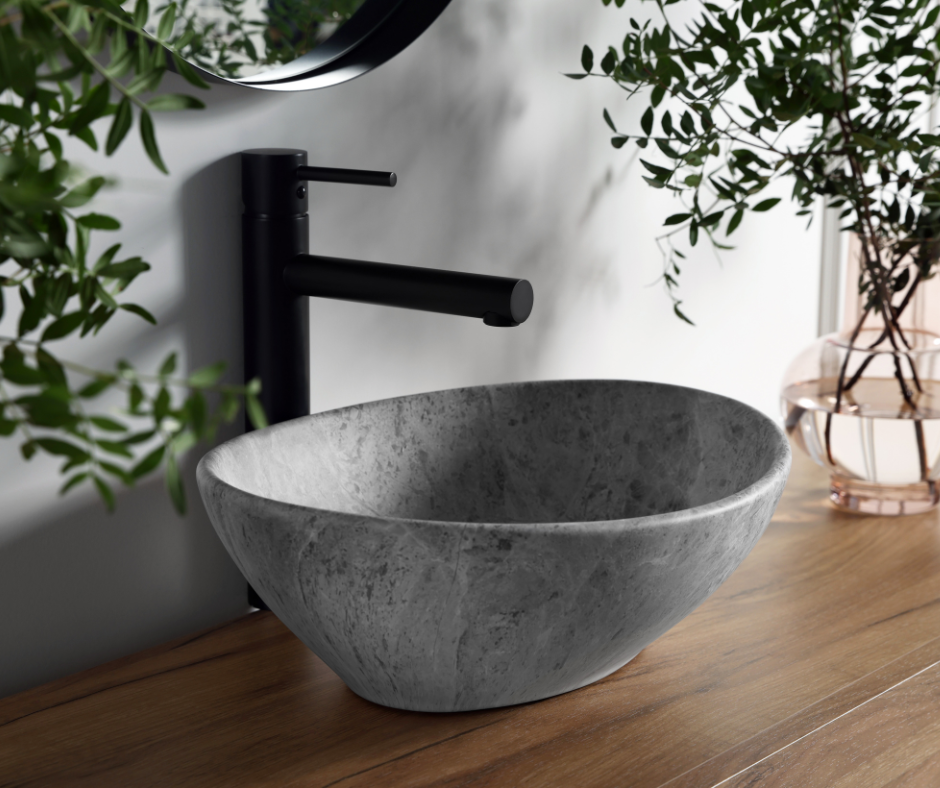 A stone sink with a black faucet and a mirror surrounded by plants