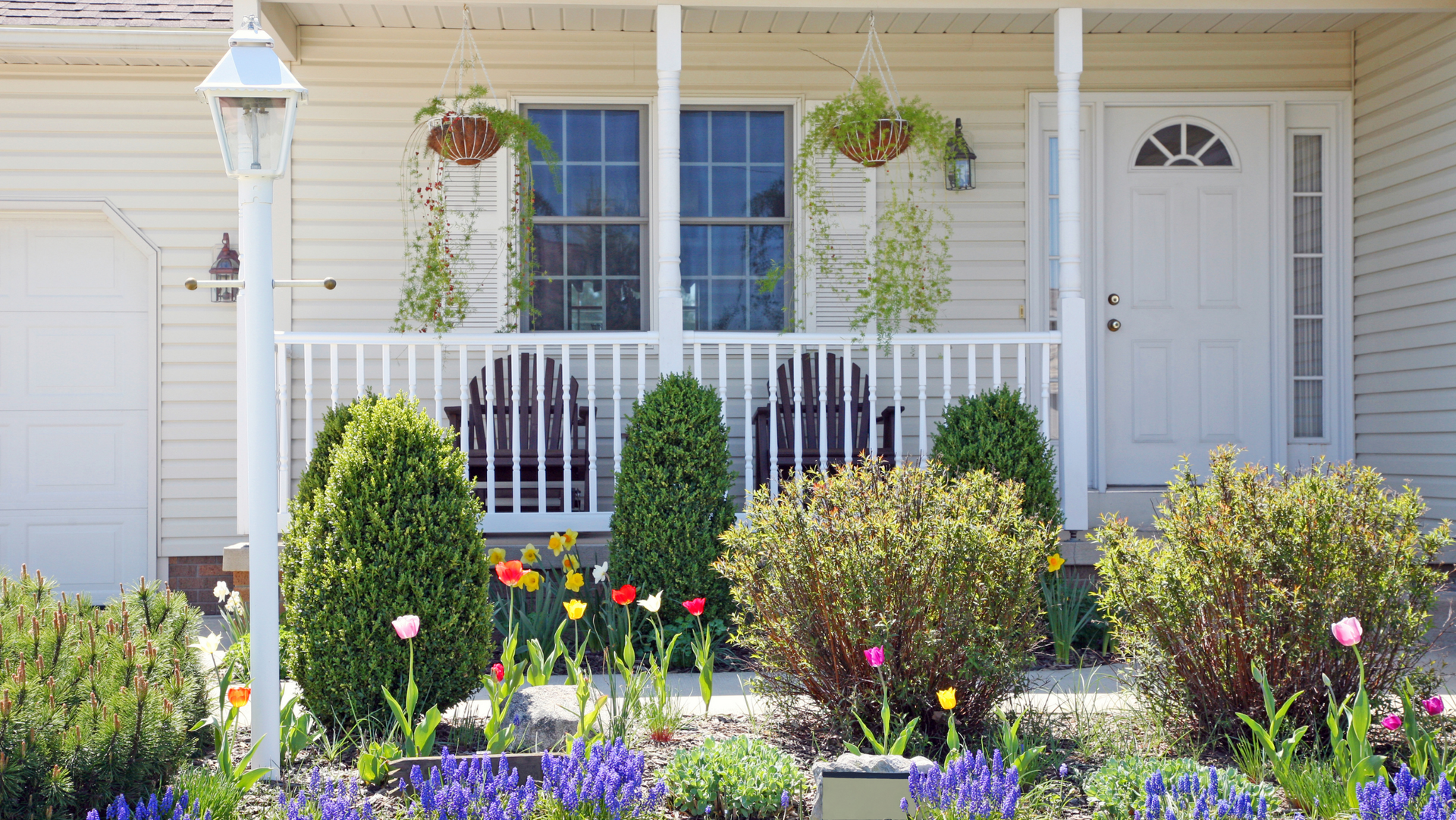 A white house in Vermont with a porch and flowers in front of it 