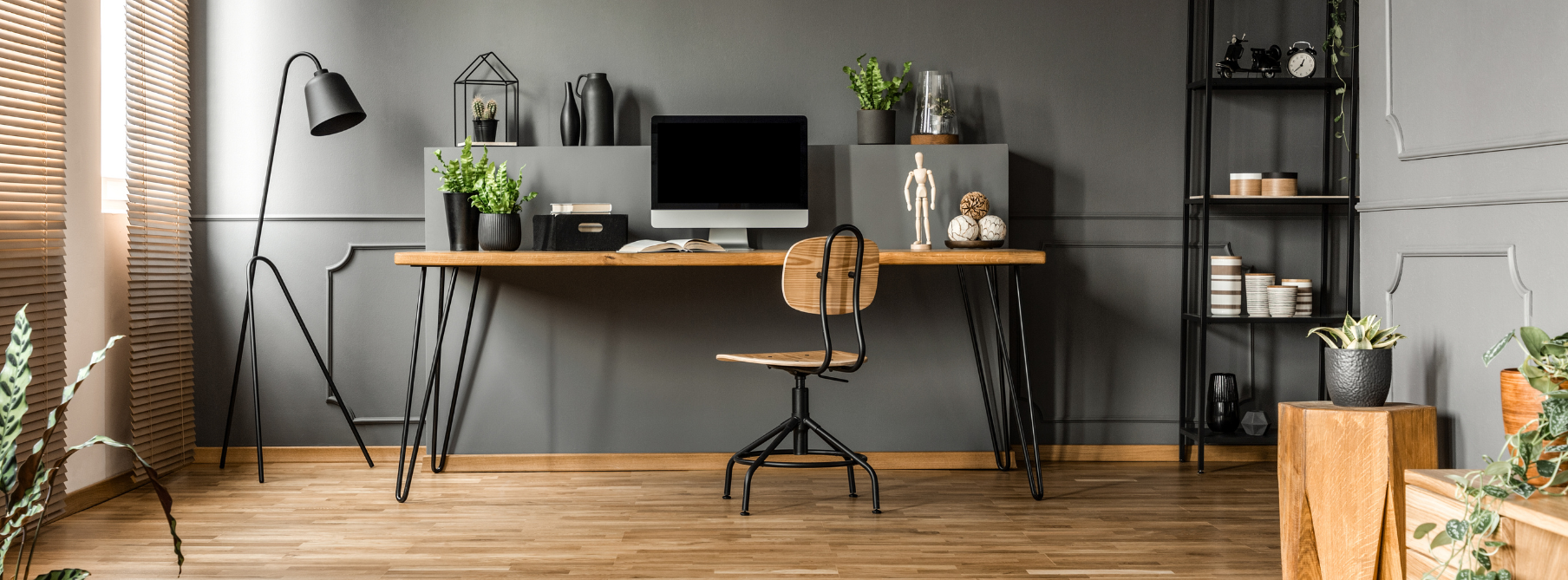 A home office with a desk, monitor, hardwood floors and desk plants