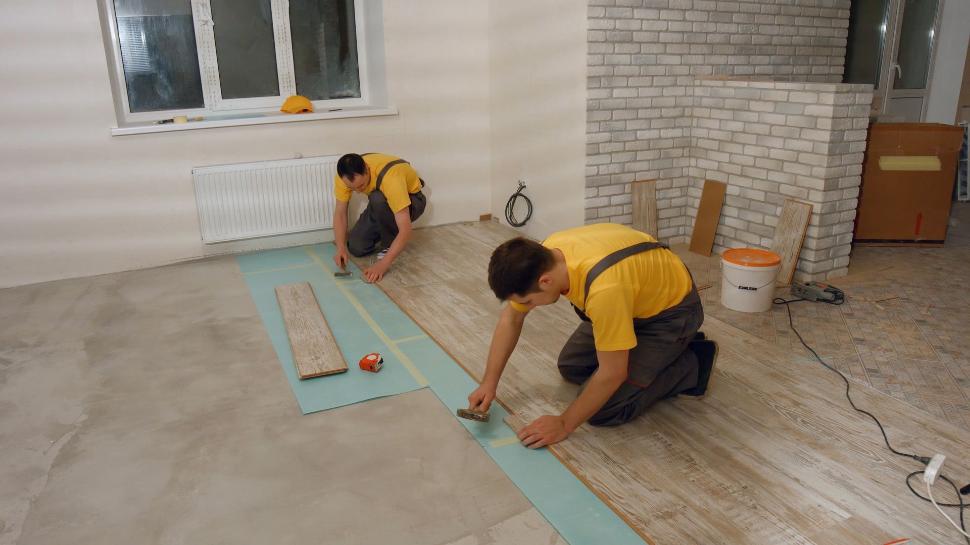Professional builders installing gray-wash laminate tile flooring during a building and renovation project