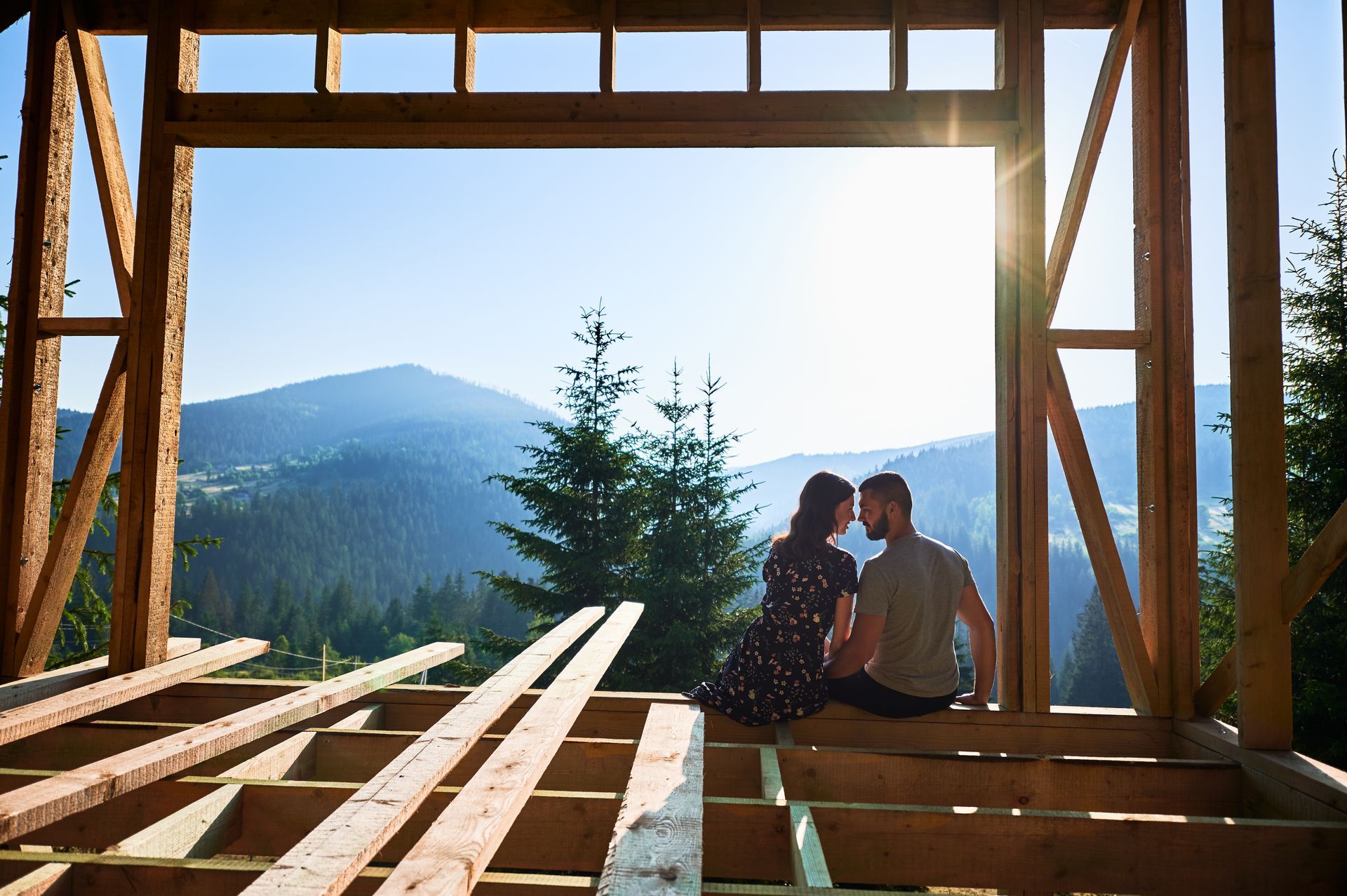 Couple sitting in framed home overlooking Vermont mountains during new home construction.