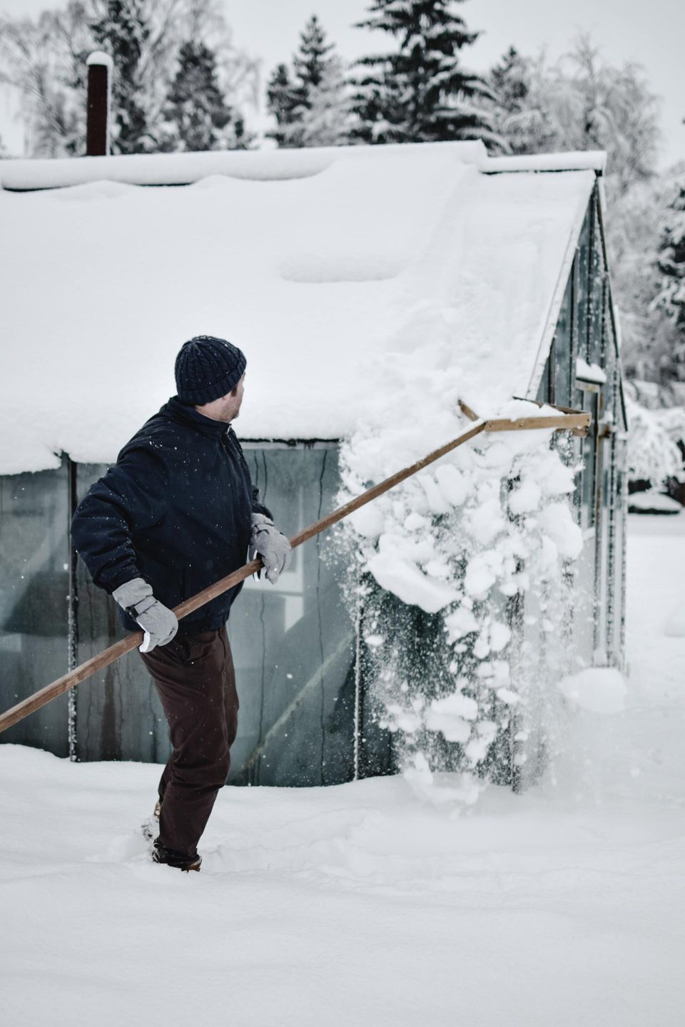 man sweeping snow off of roof with a roof rake