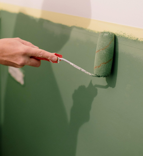 hand holding a paint brush painting a wall green