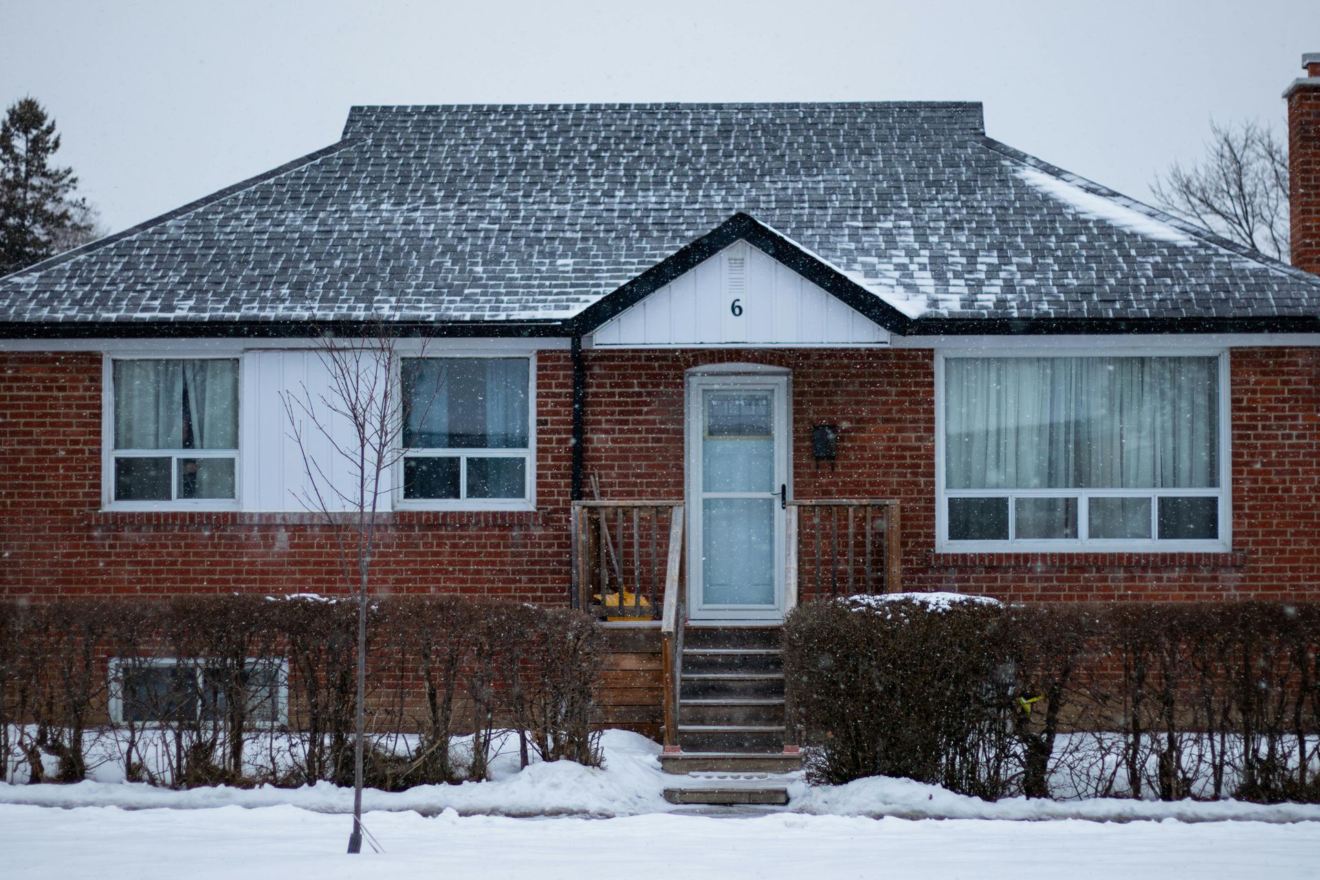 Brick house in winter snow with dark roof, windows, and front steps.