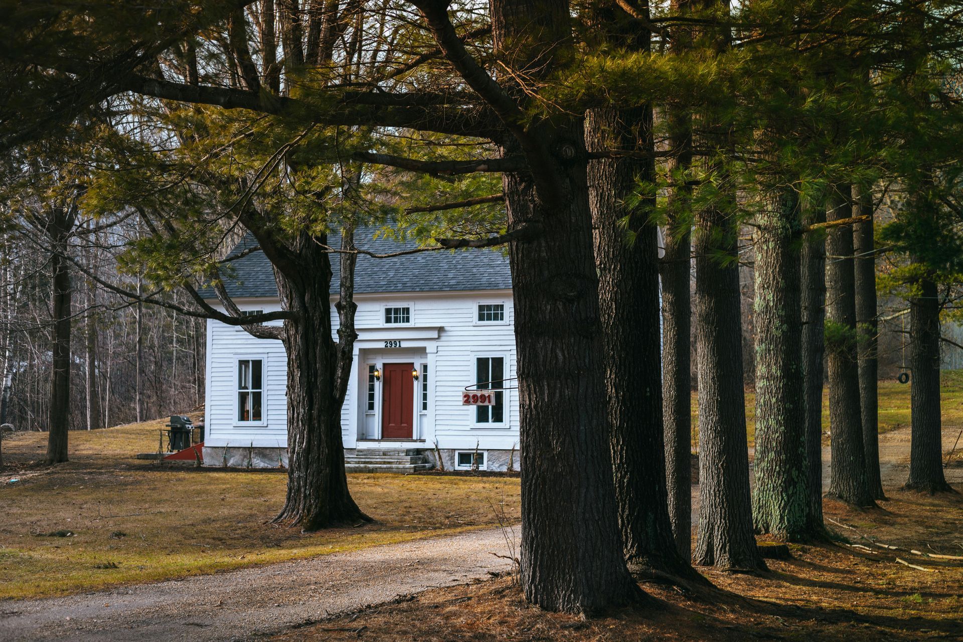 A white house with a red door is surrounded by trees