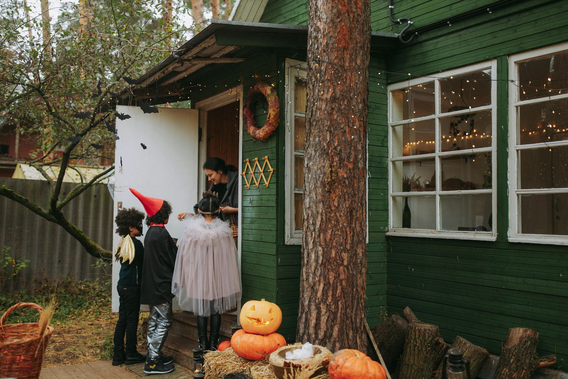 Children in Halloween costumes trick-or-treating at a green house decorated with pumpkins and lights.
