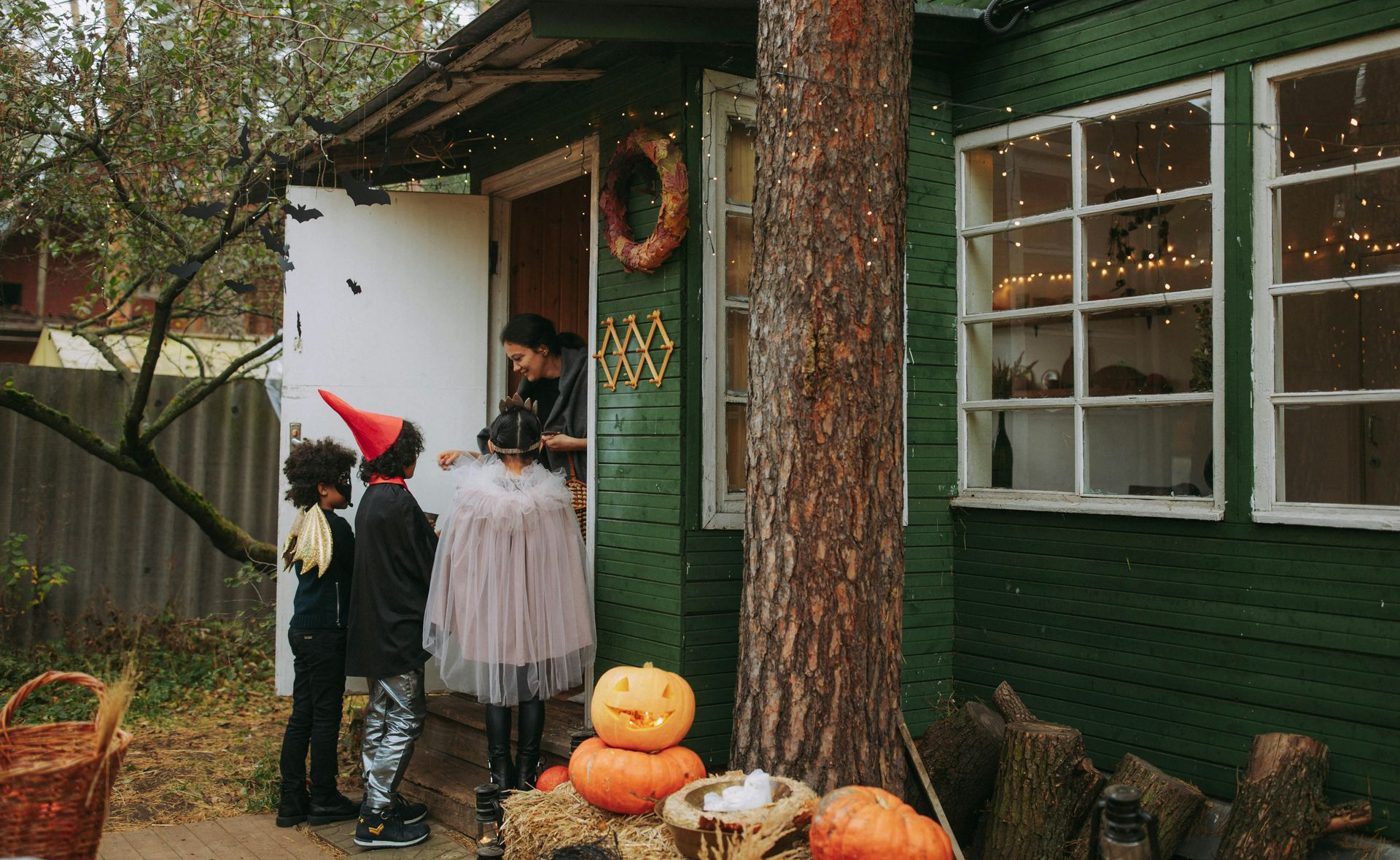 Children in Halloween costumes trick-or-treating at a green house, pumpkins on the porch.