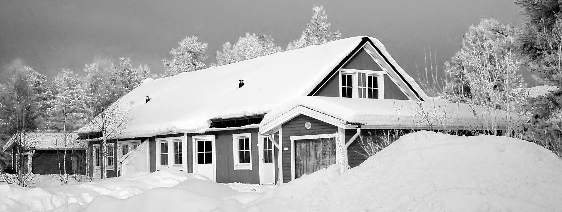 House covered in snow, snowy trees, and a large snowdrift in front.