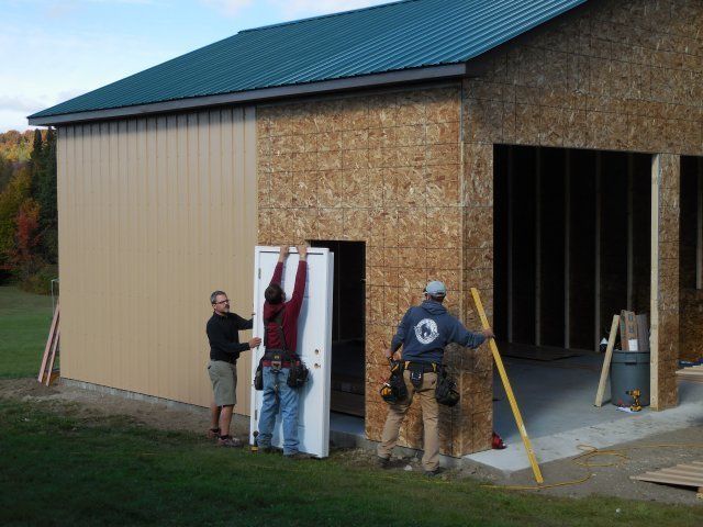 A man in a blue shirt with the letter c on the back is holding a door