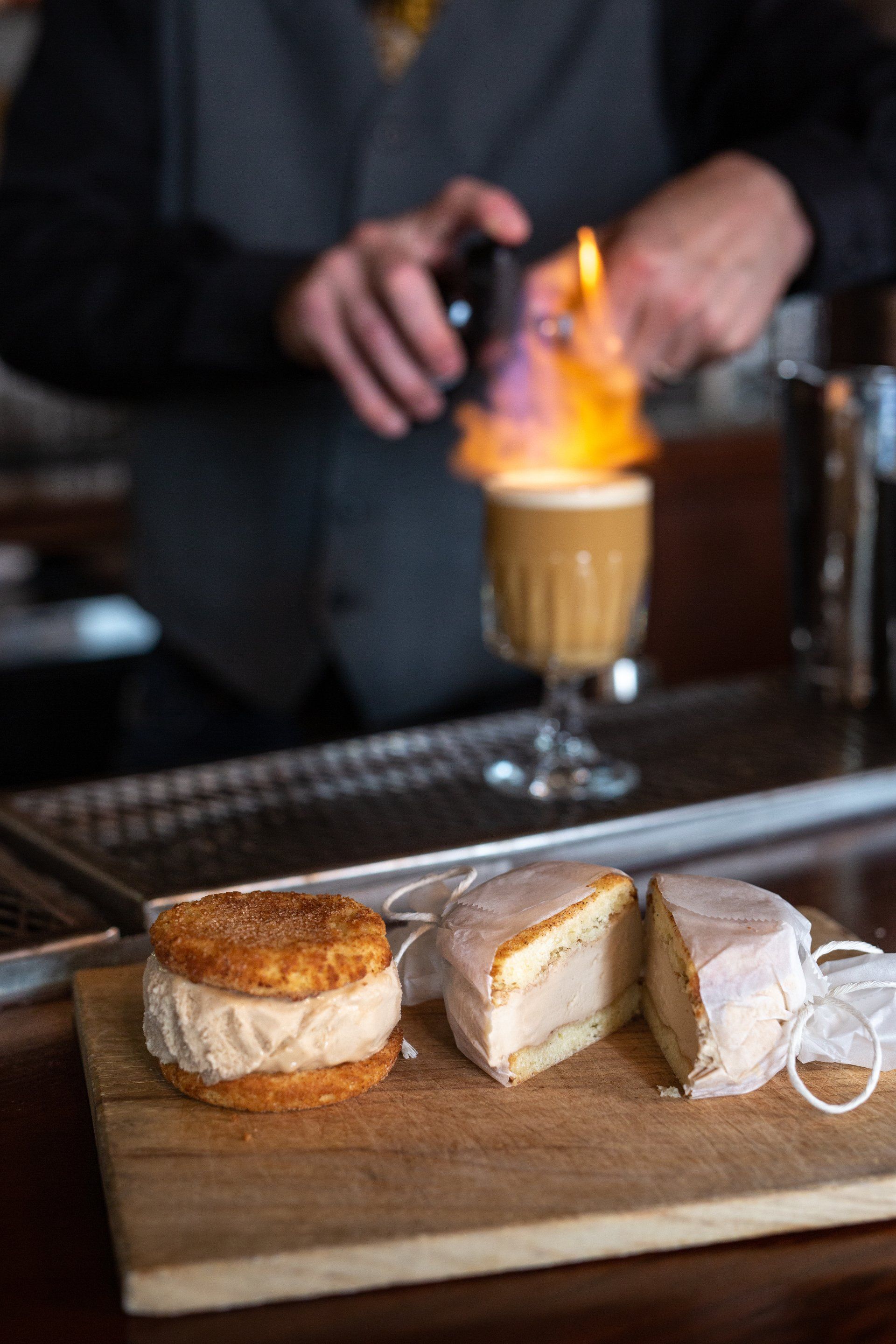 dessert on cutting board with bartender blurred out in background lighting a handcrafted cocktail on fire at planter's house st. louis